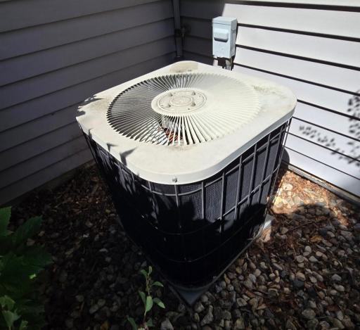 Central air unit is located in the front of the townhome behind bushes.