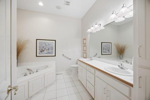 Primary bath has white tile floors, 2 sinks, jetted tub and separate shower.