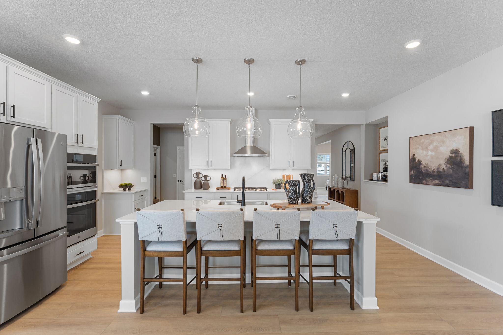At the focal point of this modern kitchen is an inviting center island that doubles as a breakfast bar, surrounded by gleaming quartz countertops and a high-end wall oven to craft delicious meals of all sizes.