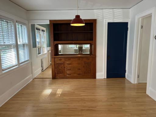 As seen from the living room, the informal dining area measures 12 x 9. Same beautiful maple flooring, with a built-in oak buffet. The open doorway camera left leads to the kitchen. The blue door opens to the stairway to the upper level.