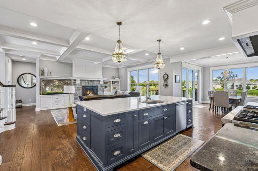 Stunning open-concept home featuring a gourmet kitchen with oversized island, coffered ceilings, stone fireplace, hardwood floors, and walls of windows overlooking scenic green space. Perfect for everyday living and entertaining.