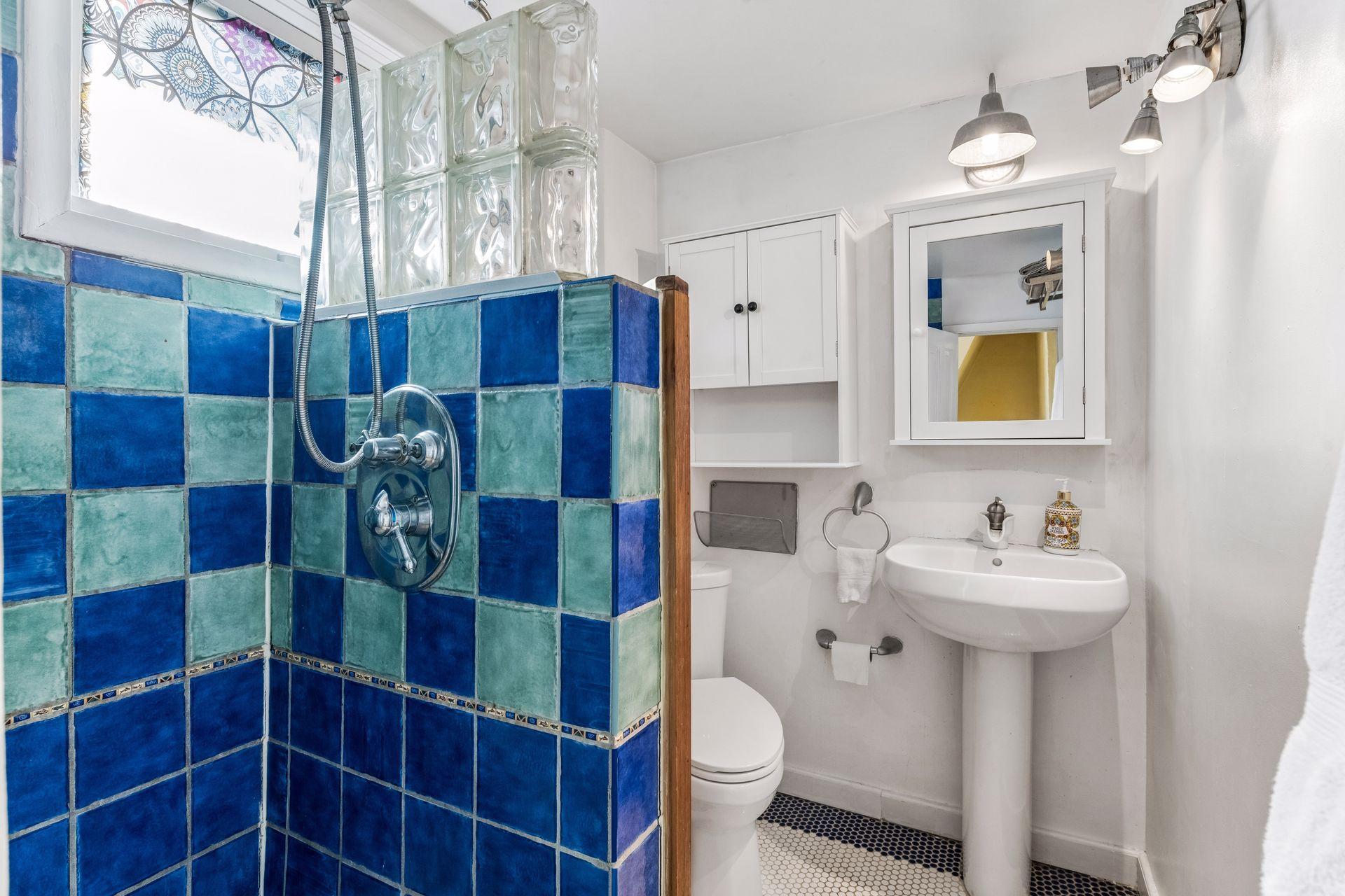 Funky, fun, and full of personality! This bathroom features vibrant blue and turquoise tile, a glass-block shower partition, classic hexagon floor tile, and a pedestal sink. A playful blend of color and character!