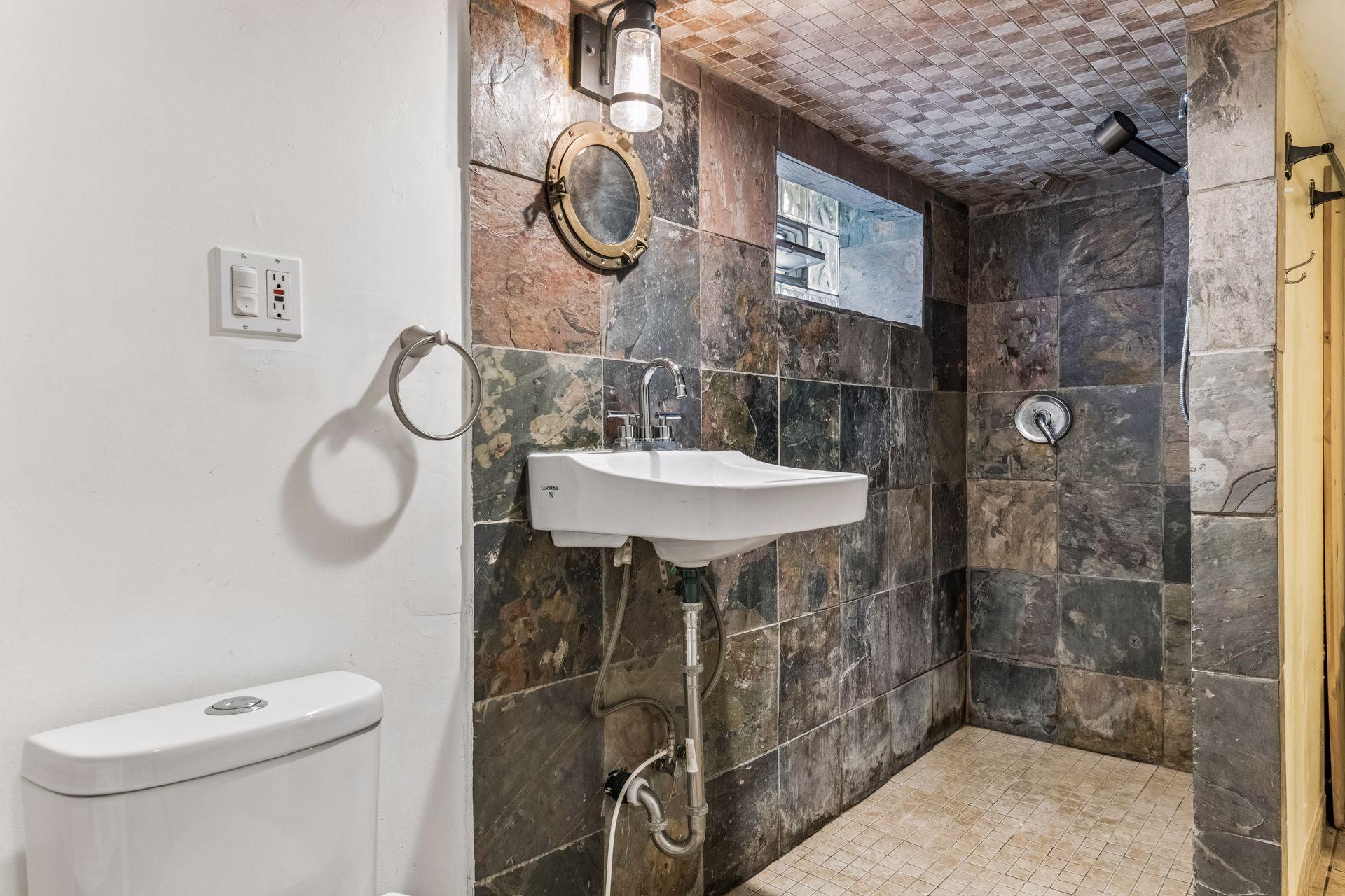The home's second ¾ bathroom is located on the lower level and features a walk-in tiled shower with natural stone finishes, a wall-mounted sink, and distinctive nautical-inspired details.