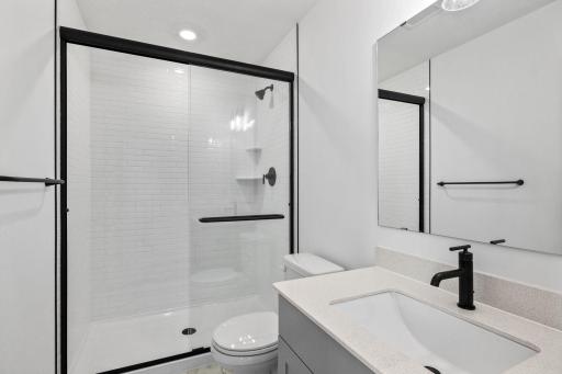 The attached bathroom includes a glass-enclosed shower with matte black trim and a quartz-topped vanity
