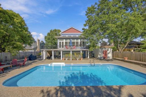 "Rear exterior showcasing the in-ground pool, wraparound deck, and heated four-season porch overlooking the backyard."