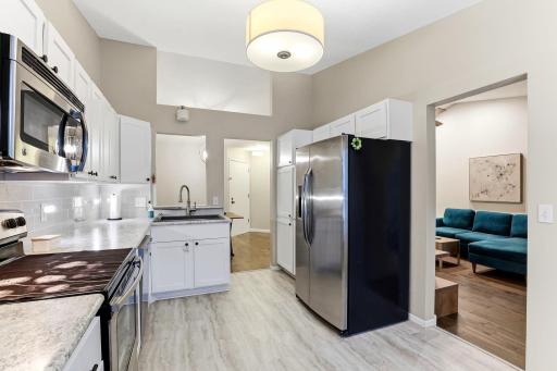 Another view of the updated kitchen showcasing abundant white cabinetry, stainless steel appliances, ample counter space, and easy flow to the living and dining areas.