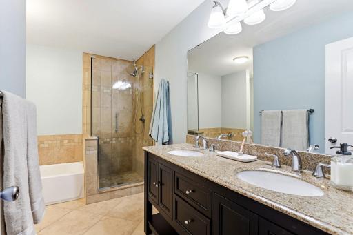Full primary bath featuring a double-sink granite vanity, tiled walk-in shower with glass enclosure, separate soaking tub, and tile flooring.