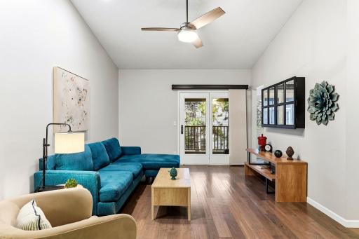Another view of the spacious living room showcasing vaulted ceilings, wood flooring, a ceiling fan, and French doors leading to the private balcony.