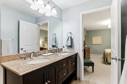 Another view of the ensuite bath showcasing the spacious double-sink granite vanity and direct access to the primary bedroom.