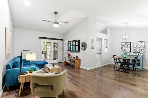 Open-concept living and dining area with vaulted ceilings, wood flooring, modern lighting, and French doors that open to the private balcony.