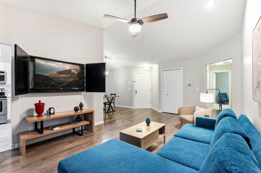 Spacious living area with vaulted ceilings and wood flooring; wall-mounted TV and TV cabinet can stay with the home.