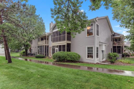 Rear exterior view showcasing private screened balconies, mature trees, lush green space, and beautifully maintained community grounds.