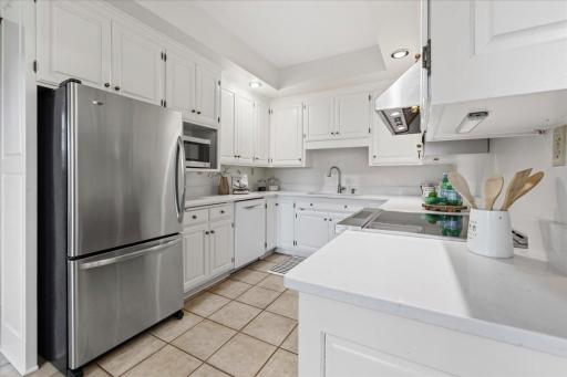 Bright kitchen offers an abundance of white cabinetry, quartz countertops, and tile floors.