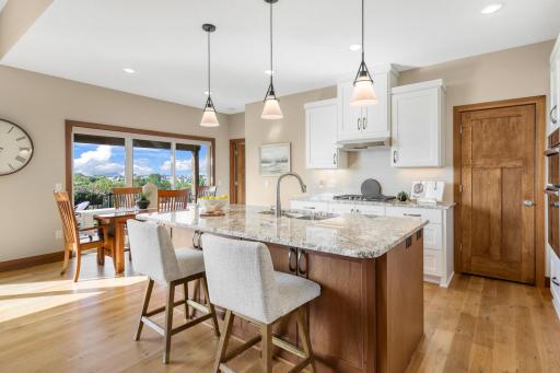 Beautifully appointed kitchen features a large granite center island with breakfast bar, contrasting cabinetry, gas cooktop, stainless appliances, pendant lighting, and an adjoining dining area with deck access.