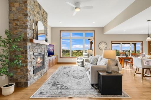 The light-filled great room features a stunning floor-to-ceiling stone fireplace, custom built-ins, hardwood floors, and expansive windows framing beautiful views.