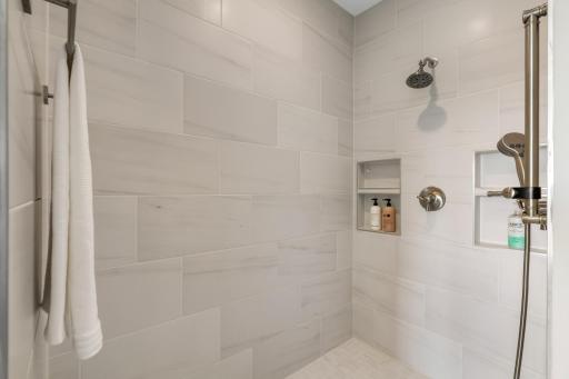 Spa-inspired walk-in shower with floor-to-ceiling tile, built-in niches, and both fixed and handheld shower heads.