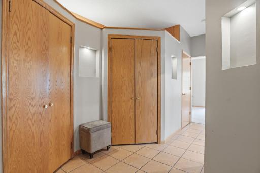 This curved lower level hallway holds a run of oak closets, tile flooring leading guests toward the finished living space just beyond.
