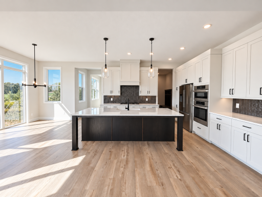 Beautifully designed kitchen featuring an oversized quartz island, contrasting cabinetry, statement pendant lighting, and abundant storage.