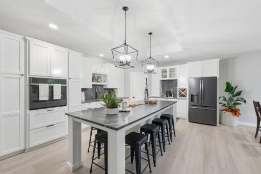 Center island with wraparound seating for six. Crisp, white cabinetry contrasted by black-slate, fingerprint-resistant SS appliances, seamlessly woven together by the strong veining on the "Charcoal Gray" granite countertops and backsplashes.