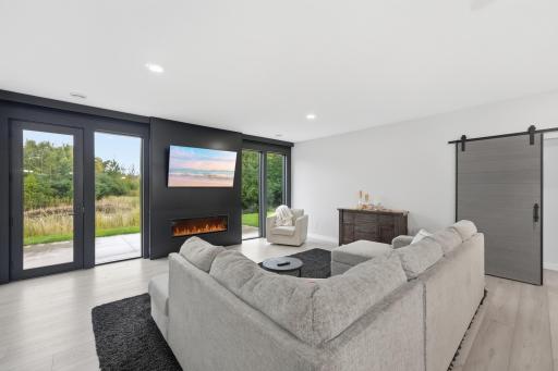 Contemporary great room showcases oversized windows, a sleek linear fireplace and dramatic dark accent wall, all overlooking the peaceful wooded and wetland setting