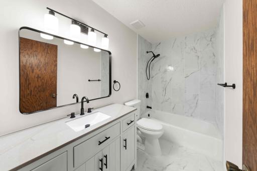 Updated full bath featuring a modern vanity, black fixtures, large mirror, and tiled flooring and shower surround