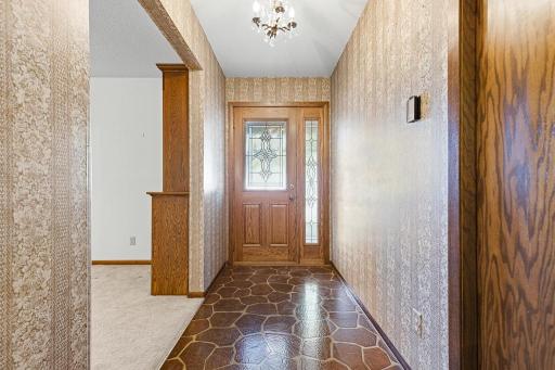 Step inside to a classic entryway featuring a hanging chandelier, solid wood door, and beveled windows