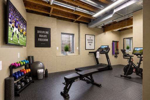Dedicated exercise space with durable flooring and wall-mounted TV, easily adaptable as a home gym, hobby room, workshop, or versatile flex space to fit your lifestyle. Virtual staging.