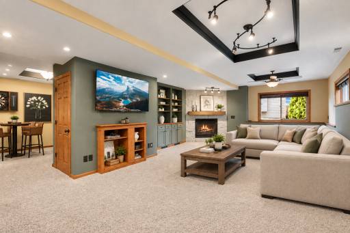 An exceptional recreation room designed for gathering, complete with custom built-in cabinetry, striking stone gas fireplace with rustic wood mantel, tray ceiling detail, and ample space for movie nights, game day, or everyday relaxation. Virtual.