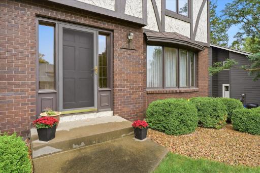 Welcoming front entrance accented by brick, mature landscaping, and charming architectural details that complement the homeâs Tudor-inspired exterior.