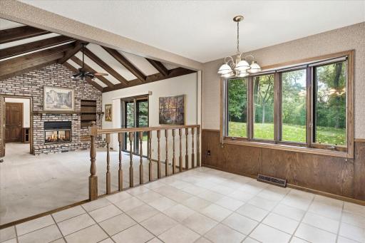 Open sightlines from the informal dining area into the impressive great room, highlighted by a dramatic vaulted beamed ceiling and brick fireplace.