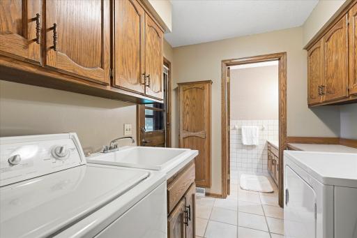 Convenient main-level laundry room features abundant cabinetry, utility sink, tile flooring, and additional counter space, plus a door leading directly to the backyard with a fenced-in dog run and easy access to the storage shed.
