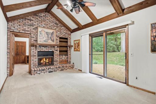 Impressive great room features a dramatic vaulted ceiling with exposed wood beams, floor-to-ceiling brick fireplace, built-in shelving, and sliding glass doors leading to the deck.