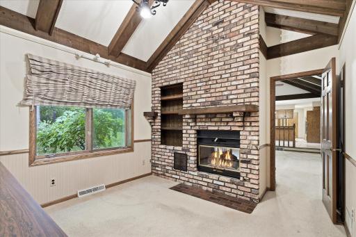 Unique main-level office features a dramatic brick fireplace with built-in shelving, vaulted beamed ceiling, and beautiful backyard views.