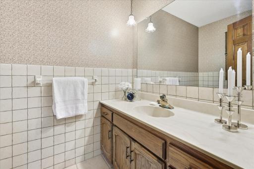 Main-level 1/2 bathroom features tile flooring, a spacious vanity, tiled walls, and a large mirror.