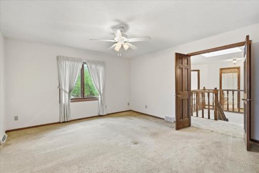 Generously sized primary bedroom features neutral finishes, a ceiling fan, large windows, and double-door entry.
