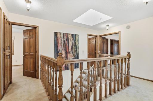 Spacious upper-level landing features warm wood railings, a skylight for added natural light, and convenient access to all 4 bedrooms.