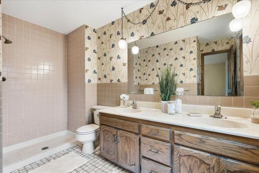 Private primary bath features a spacious double-sink vanity, large mirror, tiled flooring, and walk-in shower with tile surround.