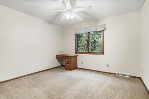 Bedroom #2: Spacious upper-level bedroom features neutral finishes, a ceiling fan, large window with views of mature trees, and a built-in desk with drawers.