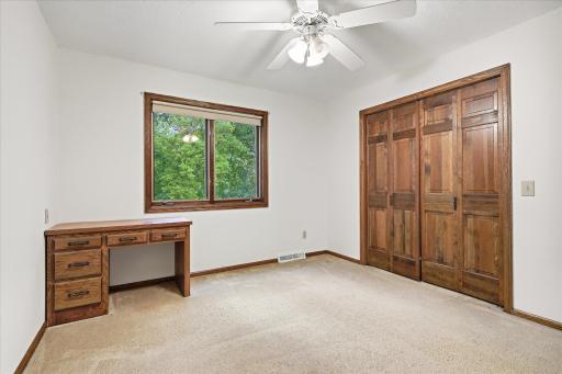 Bedroom #4: Comfortable upper-level bedroom features a ceiling fan, large window providing natural light, a built-in desk with storage, and a spacious closet with warm wood doors.