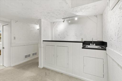 Convenient lower-level wet bar features a sink, countertop space, track lighting, and built-in storage, perfect for entertaining.