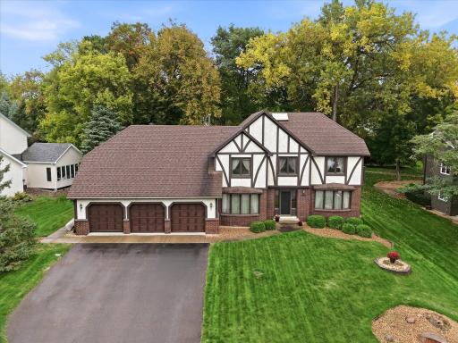 Beautiful Tudor-style exterior with a three-car garage, mature landscaping, and a spacious front lawn.