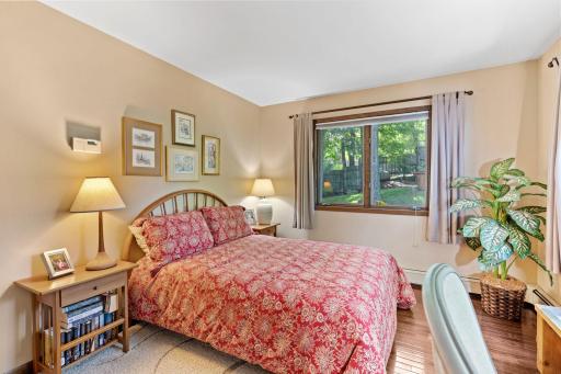 A comfortable main-level bedroom with wood floors and a quiet view of the trees.