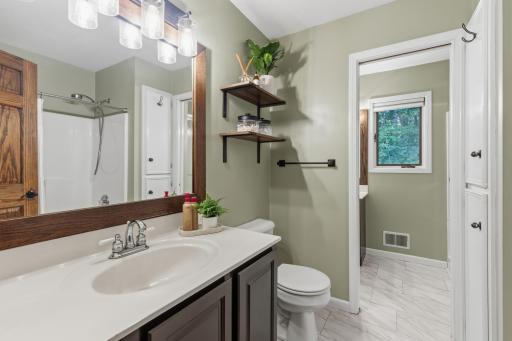 Full Walk-Through Bathroom offers a main bath that features a tub, linen closet, enameled vanity cabinet and laminate tile floors.