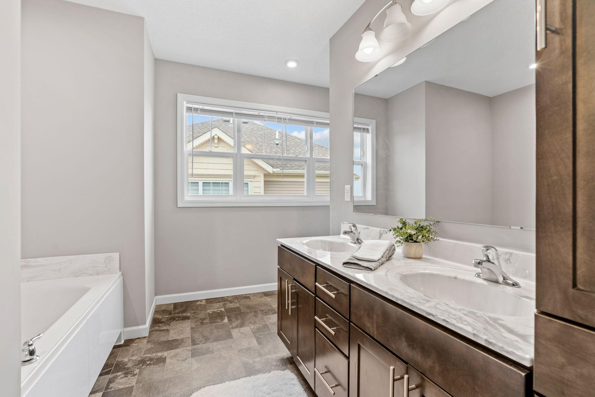 The primary bathroom has a tub, shower, dual vanity & linen cabinet