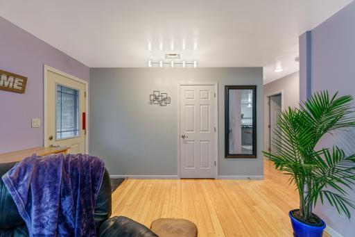 Main living room with light wood floors, track lighting, and a side entry door