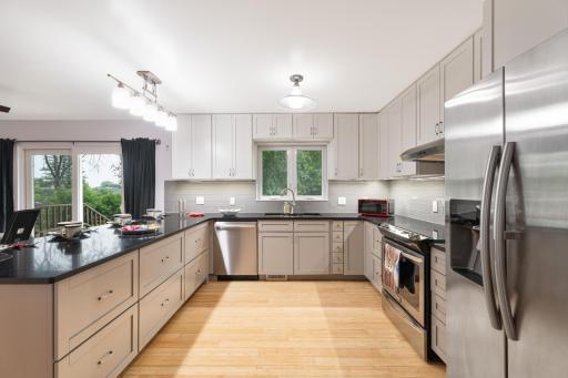 Kitchen with abundant white cabinetry, stainless appliances, window over the sink, and light wood floors