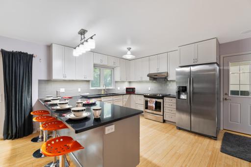 Bright, updated kitchen with white cabinetry, stainless appliances, subway tile backsplash, and a breakfast bar peninsula with seating
