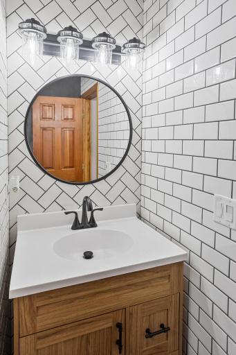 Herringbone tile, a round mirror and modern fixtures give the vanity area a fresh, polished look.