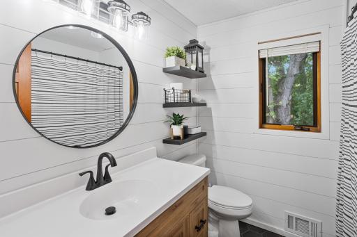 Completely updated primary bath feels fresh and inviting with shiplap walls, modern fixtures and a warm wood vanity.