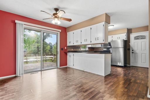 Open-concept living and kitchen area featuring laminate flooring, abundant cabinetry, stainless-steel appliances, and a large sliding glass door that fills the space with natural light and provides easy access to the deck